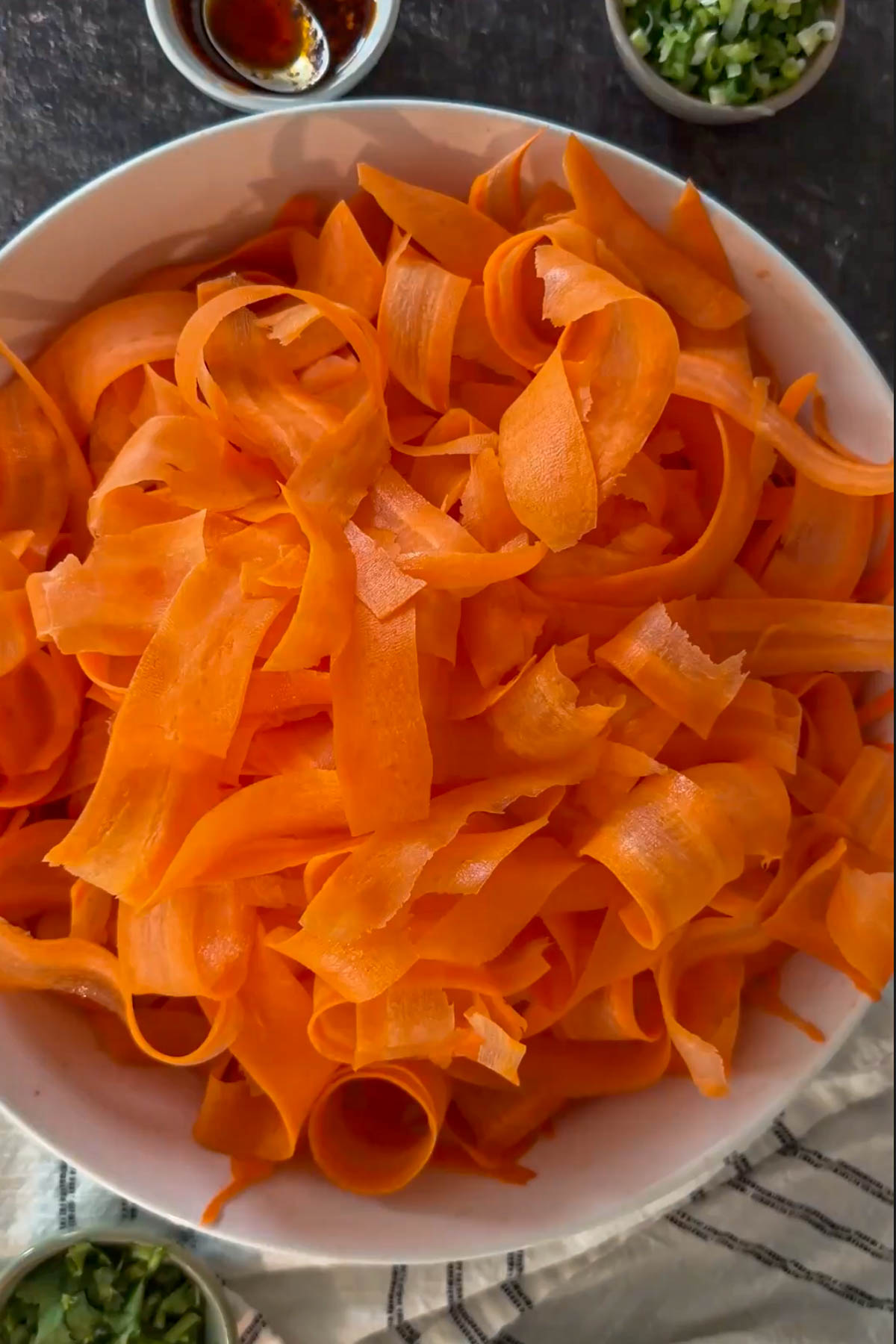 Thin carrot ribbons in a bowl before seasoning.