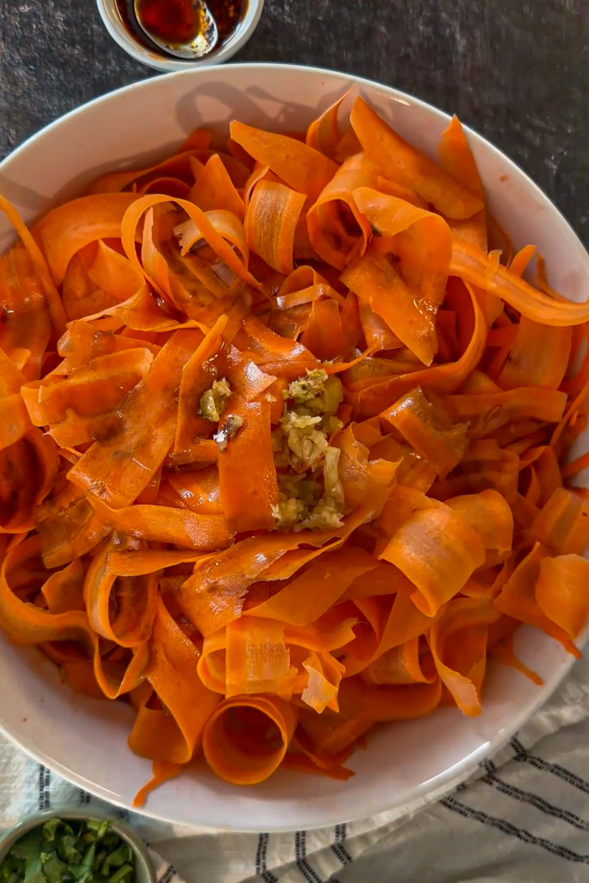 Carrot ribbons with dressing and minced garlic added to the bowl.