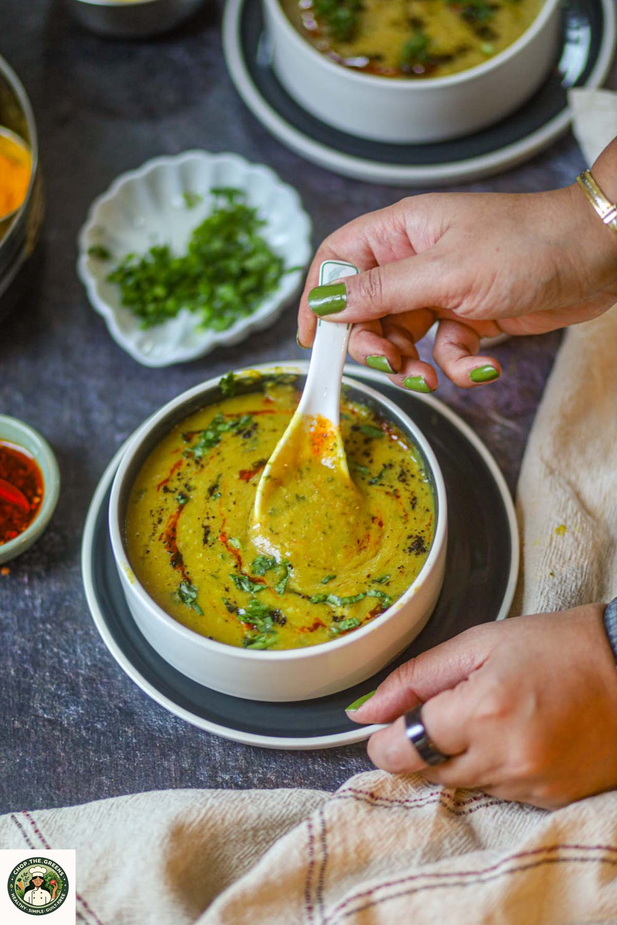 Hands holding a white bowl of creamy yellow lentil dal soup garnished with cilantro and roasted cumin.
