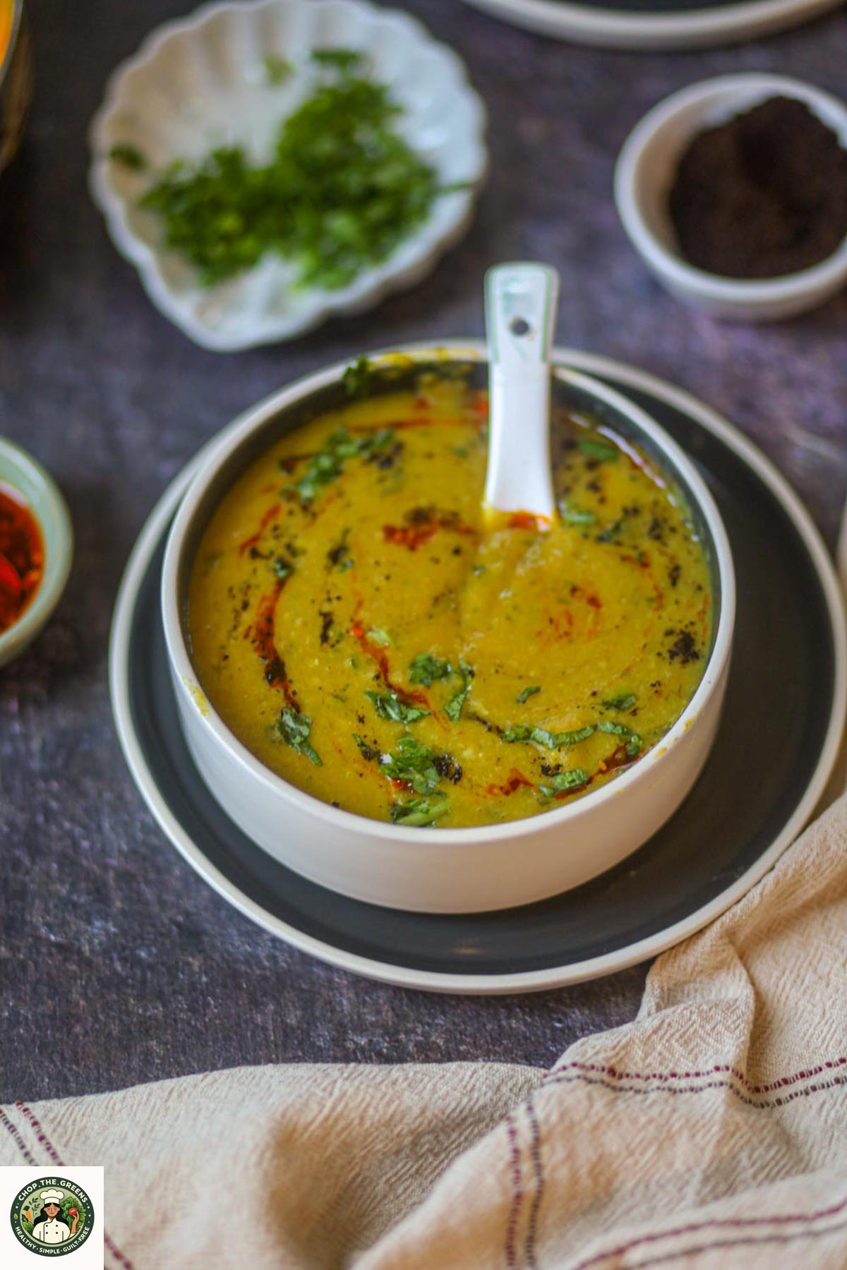 Close up of yellow lentil soup in a white bowl with a white spoon resting inside.
