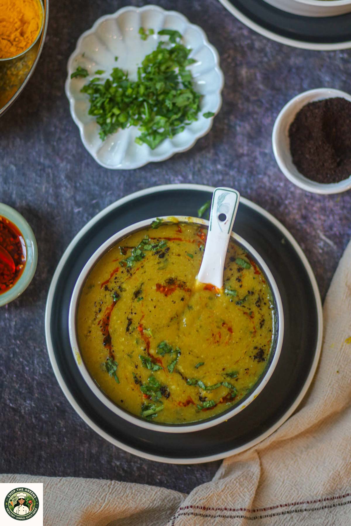 Top down view of lentil dal soup surrounded by spices like turmeric roasted cumin and fresh cilantro.
