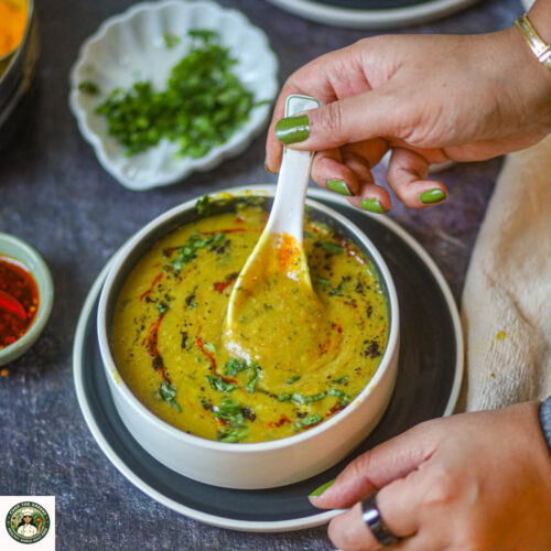 Bowl of yellow lentil soup garnished with cilantro being eaten.