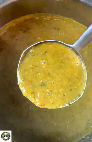 Ladle holding creamy yellow lentil soup over a pot