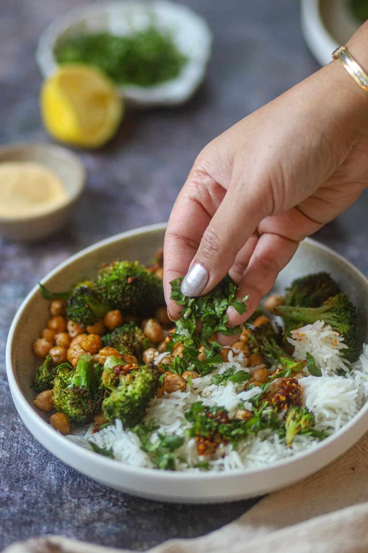 Garnishing air fryer broccoli and chickpeas with fresh herbs.