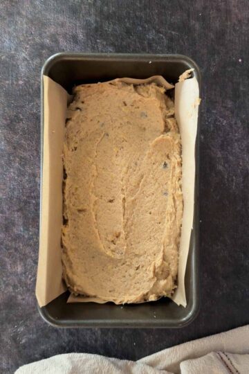 Banana bread batter spread in a lined loaf pan before baking.