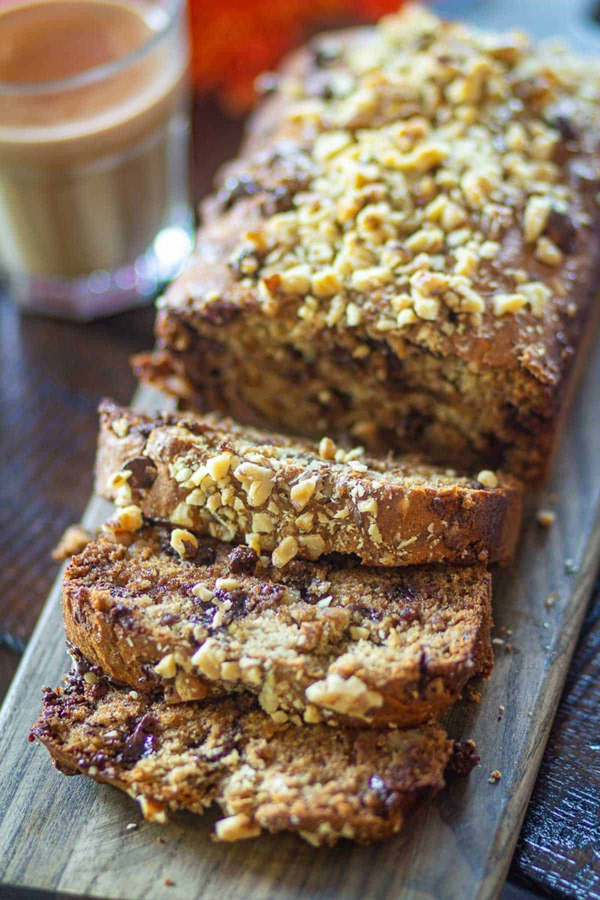Sliced eggless banana bread loaf topped with chopped nuts on a wooden board.