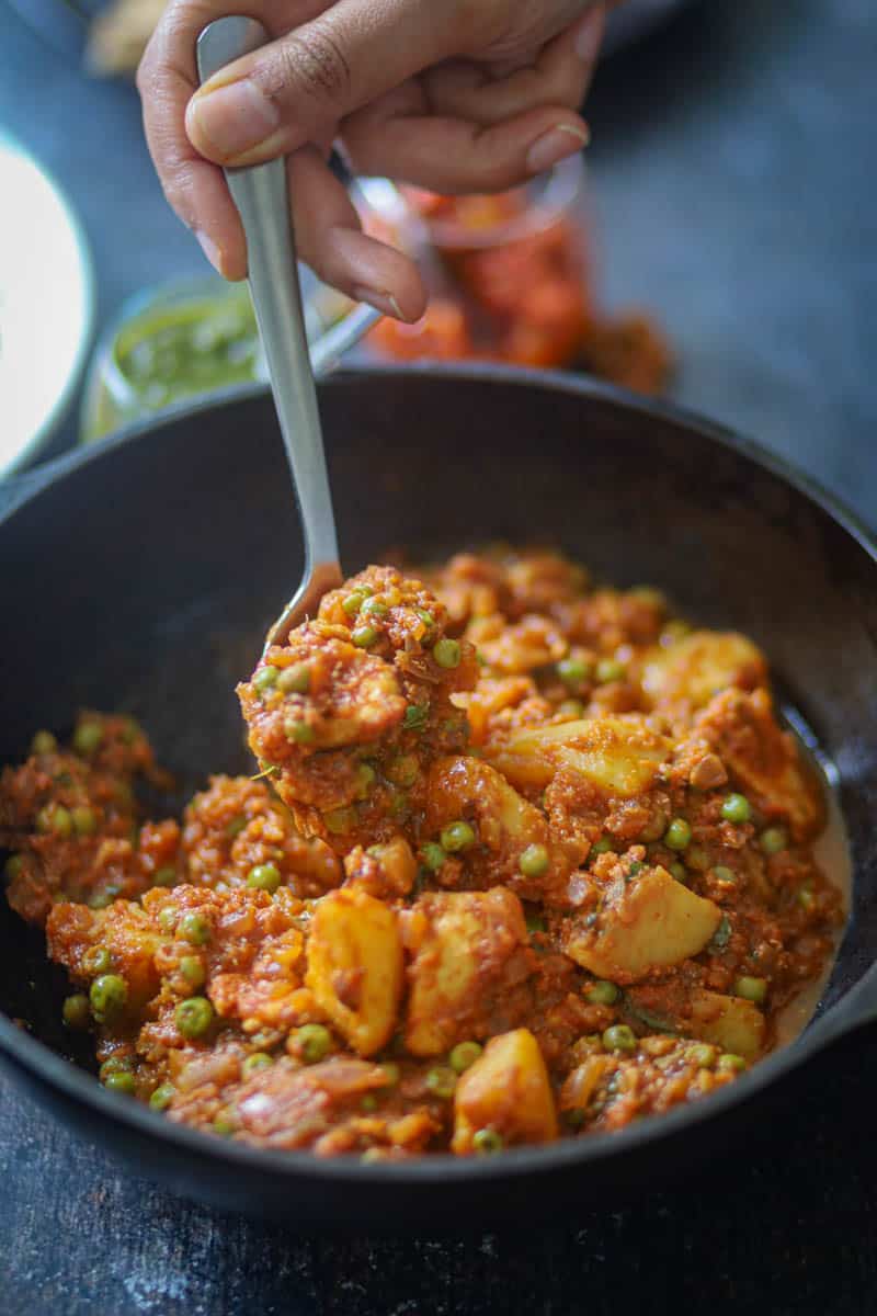 A spoonful of aloo matar paneer made in rich gravy with paneer, potatoes, and tomato based curry.