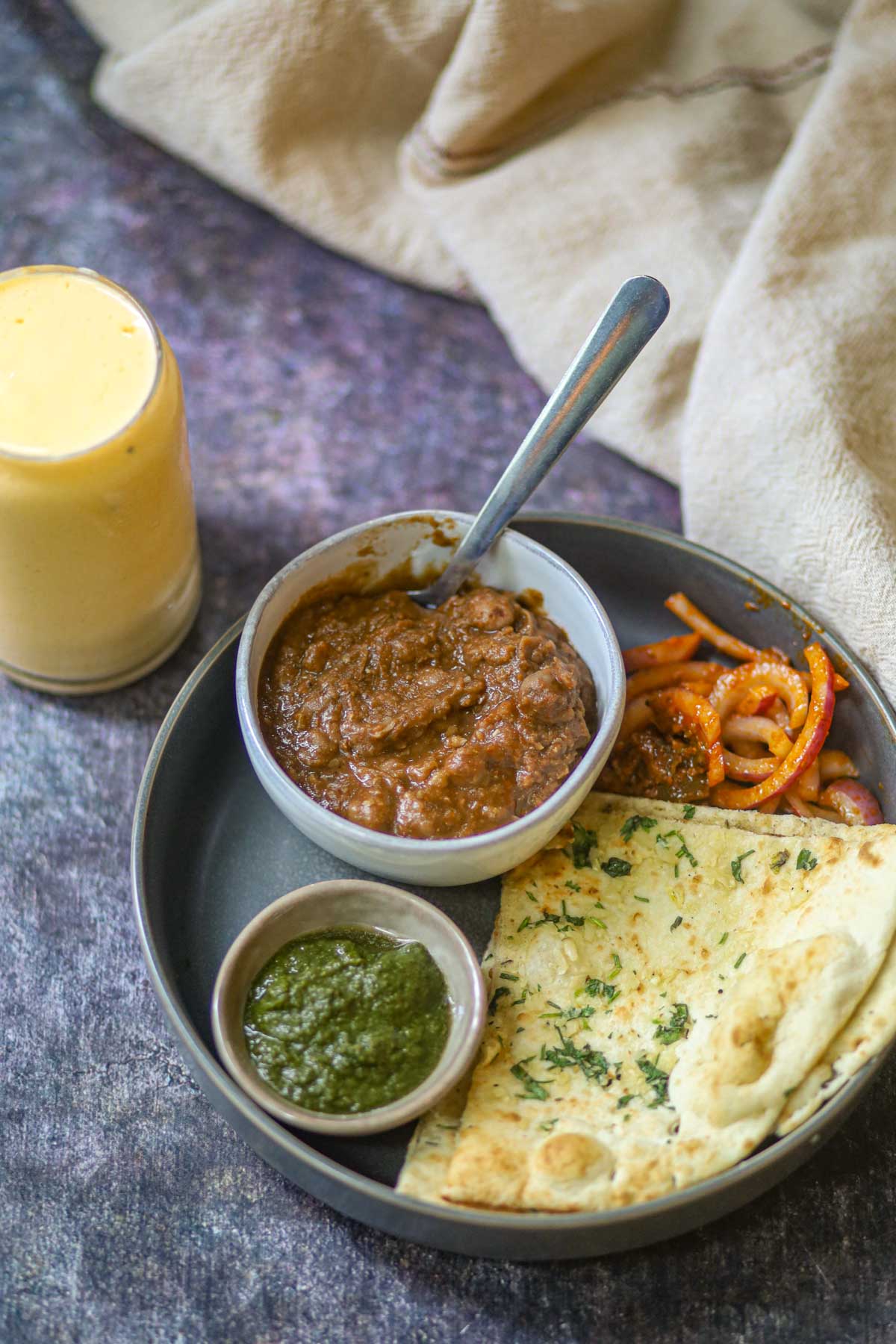 Traditional Punjabi meal with chole, garlic naan, green chutney, sautéed vegetables, and mango lassi.